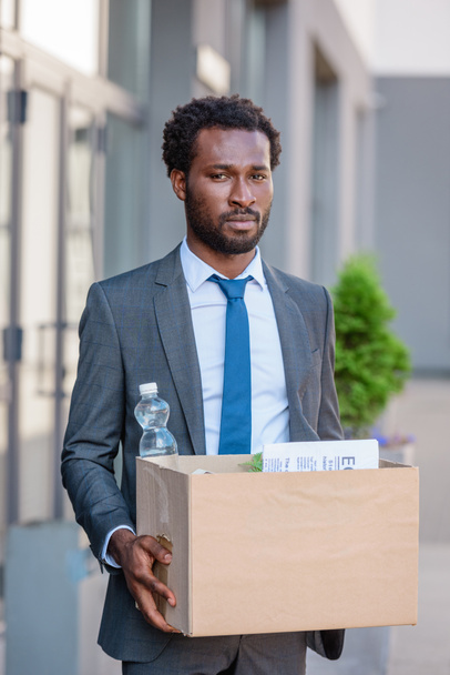 dismissed, upset african american businessman holding carton box and looking at camera - Фото, зображення