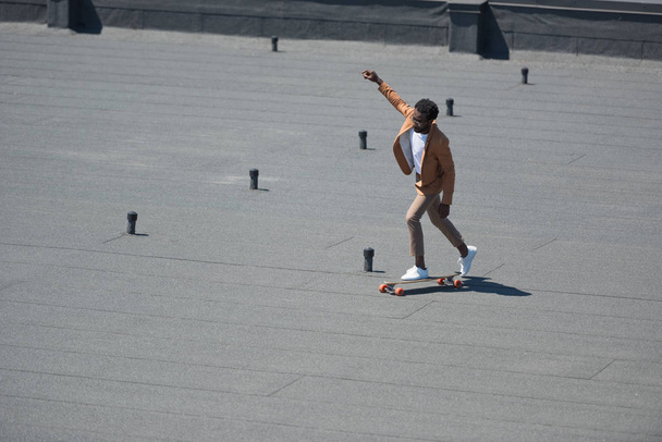 stylish african american businessman riding lonboard on sunny rooftop - Фото, зображення