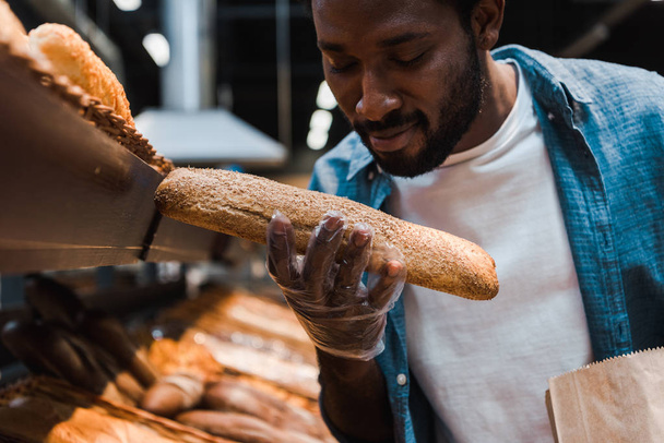 επιλεκτική εστίαση του Happy Αφρικανός Αμερικανός άνθρωπος κοιτάζοντας φρέσκο ψωμί στο σούπερ μάρκετ  - Φωτογραφία, εικόνα