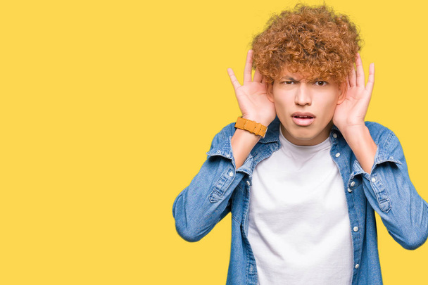 Young handsome man with afro hair wearing denim jacket Trying to hear both hands on ear gesture, curious for gossip. Hearing problem, deaf - Photo, Image