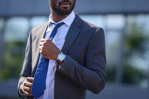 abgeschnittene Ansicht eines afrikanisch-amerikanischen Geschäftsmannes, der Krawatte berührt, während er auf der Straße steht - Foto, Bild
