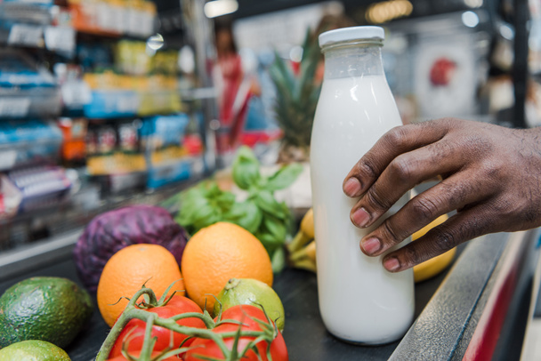 levágott kilátás afroamerikai férfi gazdaság üvegpalack tejjel közelében szupermarket számláló  - Fotó, kép