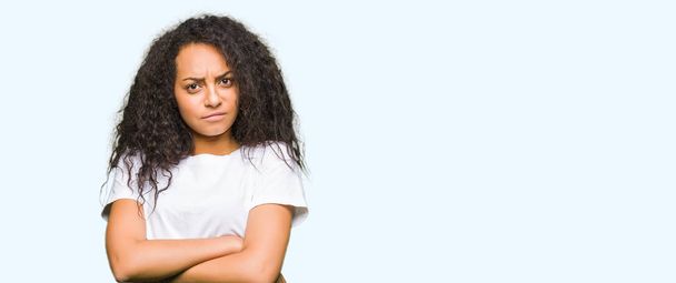 Young beautiful girl with curly hair wearing casual white t-shirt skeptic and nervous, disapproving expression on face with crossed arms. Negative person. - Foto, Imagem