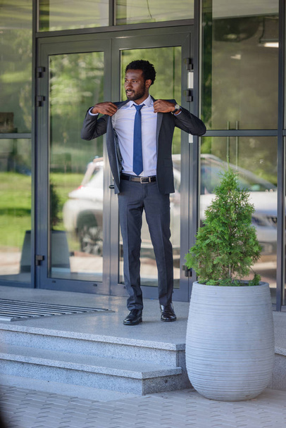 オフィスビルの近くに立っている間、スーツを着たハンサムなアフリカ系アメリカ人ビジネスマン - 写真・画像
