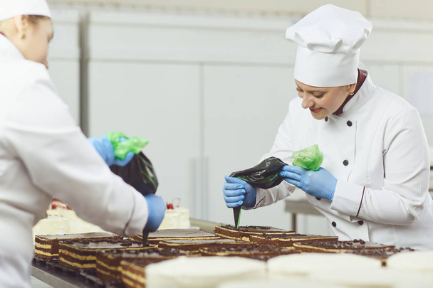A confectioners squeezes liquid cream from a pastry bag. - Фото, изображение