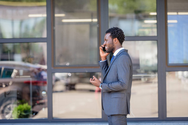 allegro uomo d'affari afro-americano che parla su smartphone mentre si trova vicino all'edificio degli uffici
 - Foto, immagini