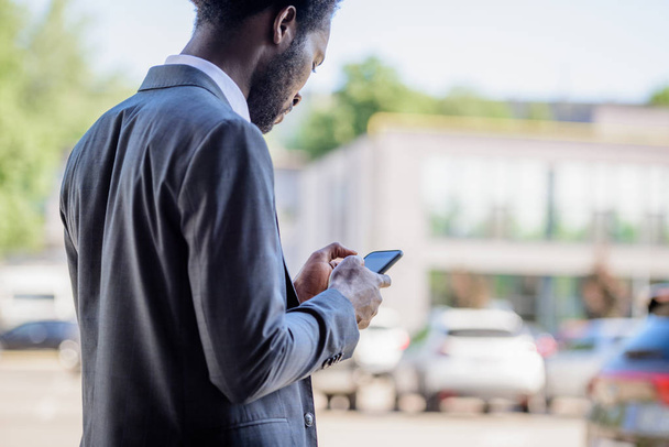 serious african american businessman in suit using smartphone on street - Zdjęcie, obraz