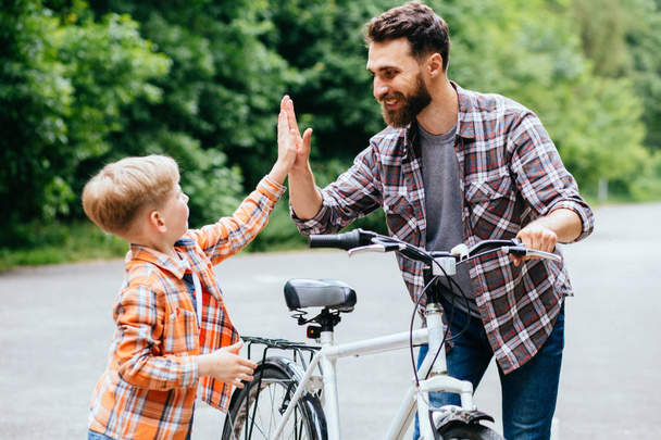 Father and son give high five while cycling in the park - Photo, Image