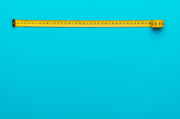 Top view of yellow measuring tape over turquoise blue background with copy space - Фото, зображення