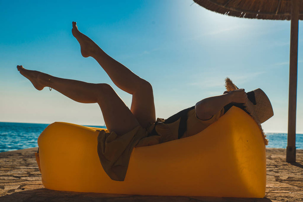 woman in yellow sundress laying at yellow sofa at sea beach - Photo, Image