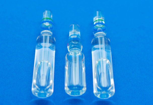 Tres ampollas de vidrio con solución para un primer plano infeccioso sobre un fondo azul
. - Foto, imagen