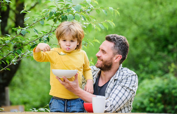 Summer breakfast. Healthy food concept. Feeding baby. Menu for children. Family enjoy homemade meal. Father son eat food and have fun. Food habits. Little boy with dad eating food nature background - 写真・画像