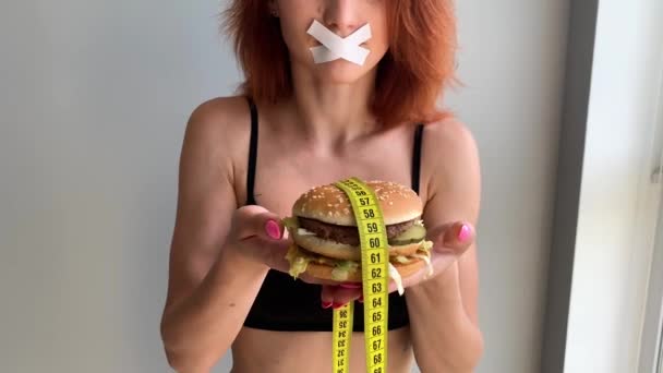 Diyet. Bir kadının portresi bir burger yemek istiyor, ama bir yapıştırılmış ağız, diyet kavramı, sağlıksız gıda, beslenme bir irade - Video, Çekim