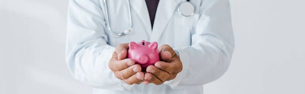 Panoramaaufnahme des Arztes mit rosa Sparschwein in der Hand auf weiß - Foto, Bild