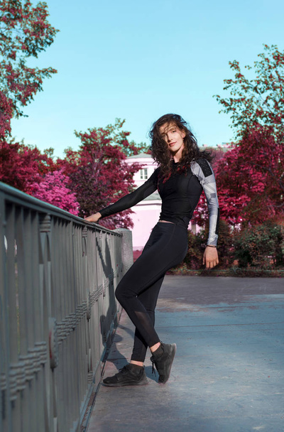 girl with wavy hair in sports clothes on the bridge in the Park  - Φωτογραφία, εικόνα