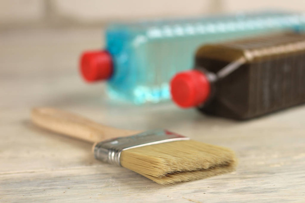 Une brosse se trouve à côté de bouteilles en plastique avec tache et solvant sur une vieille table en bois vintage blanc. Lieu pour le texte ou le logo
. - Photo, image