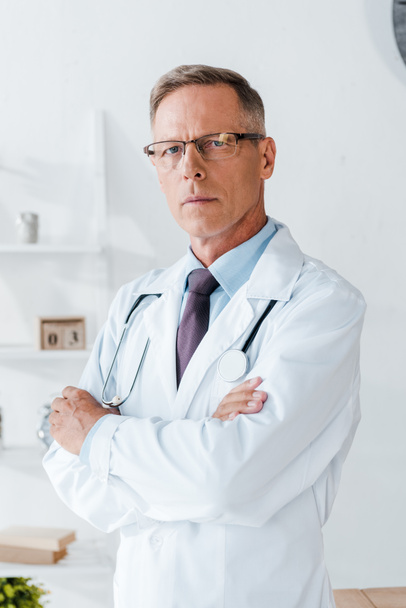 serious doctor in glasses and white coat standing with crossed arms  - Фото, изображение