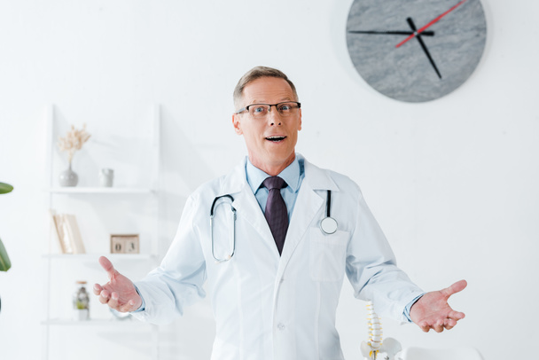 удивленный доктор в белом халате и очках жестом в клинике
  - Фото, изображение