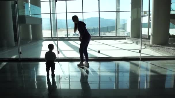 Mom and small boy go to the window at the airport hall to look at the plane - Footage, Video