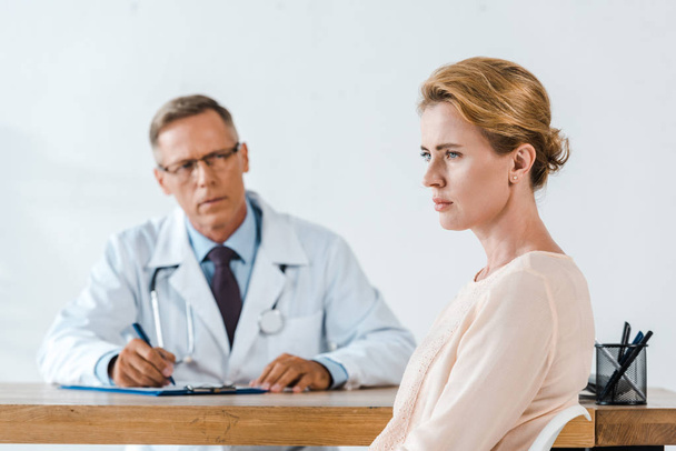 foco seletivo da mulher chateada sentada perto do médico de casaco branco
  - Foto, Imagem