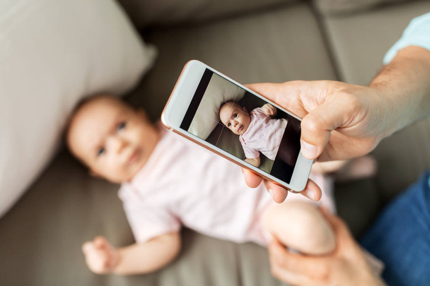 father with smartphone taking picture baby at home - Foto, imagen