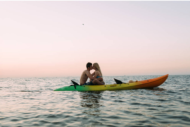 Ocean coast, a loving couple sitting on a kayak in the water and kissing - Photo, Image
