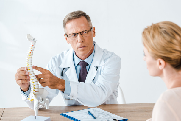 selective focus of doctor in glasses pointing with finger at spine model near woman  - Φωτογραφία, εικόνα