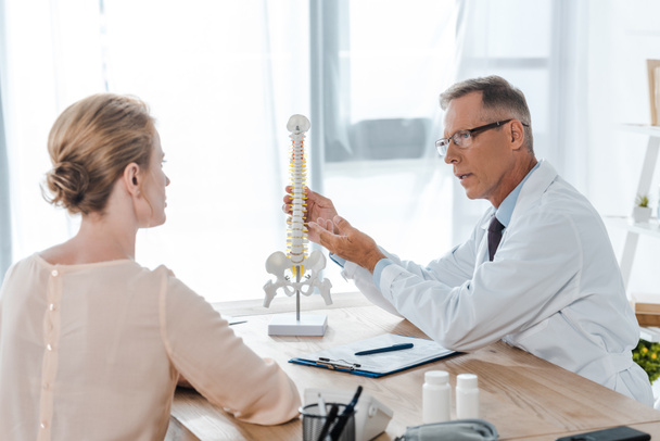 selective focus of doctor in glasses touching spine model near patient - Foto, Bild