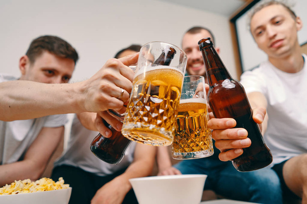 Vrienden kijken tv tijdens het eten chips popcorn en het drinken van wat koud bier - Foto, afbeelding