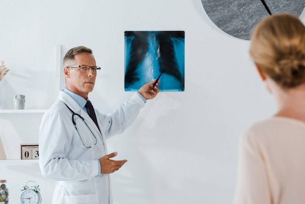 foyer sélectif du médecin dans les lunettes tenant le stylo près de rayons X et la femme à la clinique
  - Photo, image