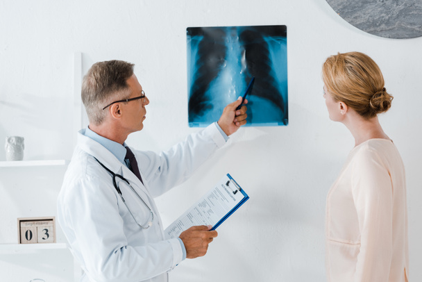 doctor in glasses holding pen near x-ray and patient in clinic  - Photo, Image