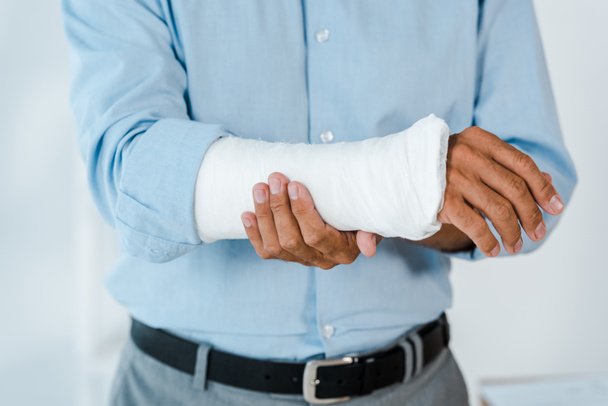 cropped view of injured man touching broken arm wrapped in gypsum bandage  - Foto, Imagem