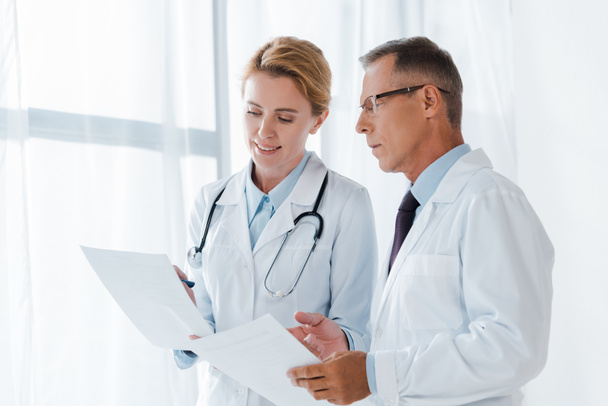 cheerful doctor holding paper near handsome coworker in glasses  - Foto, imagen
