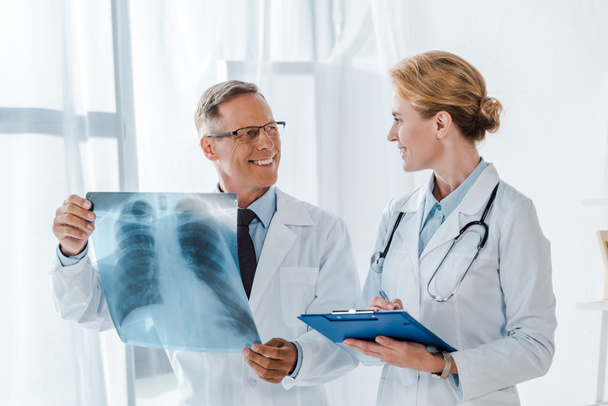 szczęśliwy lekarz trzyma schowek i patrząc na wesoły współpracownika z x-ray  - Zdjęcie, obraz