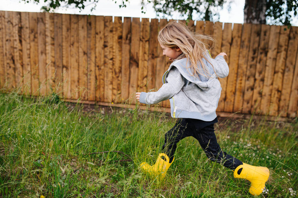Very happy little boy is running fast in yellow rubber boots - Fotoğraf, Görsel