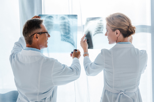 médico feliz em óculos e belo colega de trabalho segurando raios-x na clínica
  - Foto, Imagem