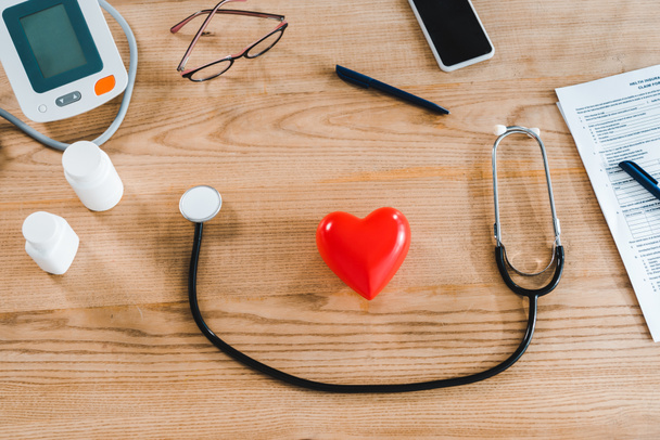 pohled na stetoskop v blízkosti modelu červeného srdce a smartphone s prázdnou obrazovkou  - Fotografie, Obrázek