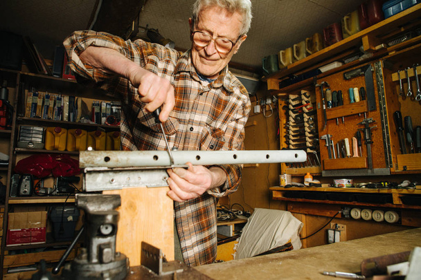 Amateur senior carpenter at his workbench, fastening holed metal strips - Fotoğraf, Görsel