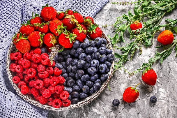 Корзина со свежими ягодами на бетонном фоне - летний сбор ягод
.  - Фото, изображение