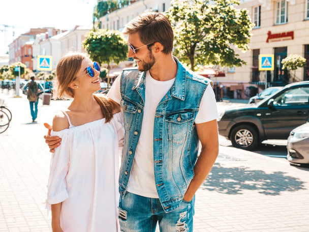 Smiling beautiful girl and her handsome boyfriend. Woman in casual summer dress and man in jeans clothes. Happy cheerful family. Female having fun on the street background.Hugging couple in sunglasses - Fotoğraf, Görsel