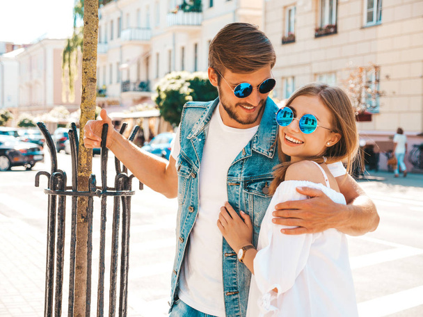 Smiling beautiful girl and her handsome boyfriend. Woman in casual summer dress and man in jeans clothes. Happy cheerful family. Female having fun on the street background.Hugging couple in sunglasses - Zdjęcie, obraz