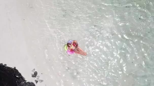 Mavi tropikal okyanus gölündeki lilo şişme yatağında güneşlenen genç bir kadının hava manzarası.  - Video, Çekim