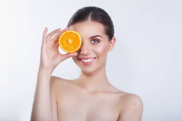 Funny girl holding orange in front of her face and showing tongue on white background. - Foto, afbeelding