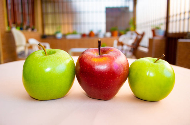 Два зелених яблука і червоне яблуко в центрі видно спереду з красивим садом на задньому плані
. - Фото, зображення
