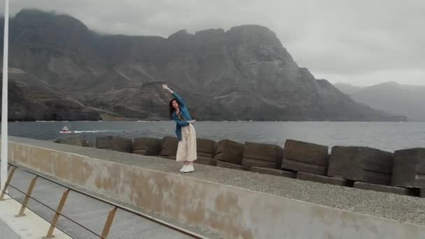 Aerial view - a young woman tourist fooling around against the background of the ocean and the misty mountains. Agaete, Gran Canaria - Кадры, видео