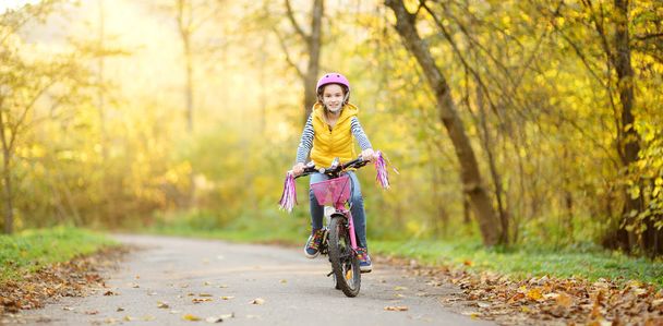 Adorable young girl riding a bike in a city park on sunny autumn day. Active family leisure with kids. - Photo, Image