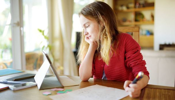Smart preteen schoolgirl doing her homework with digital tablet at home. Child using gadgets to study. - Fotó, kép