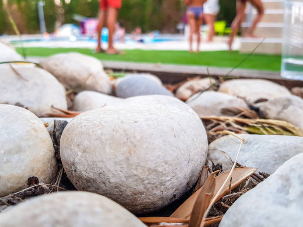 Στρογγυλεμένες πέτρες κήπου στο προσκήνιο και εκτός εστίασης παιδιά που παίζουν στο φόντο της πισίνας - Φωτογραφία, εικόνα