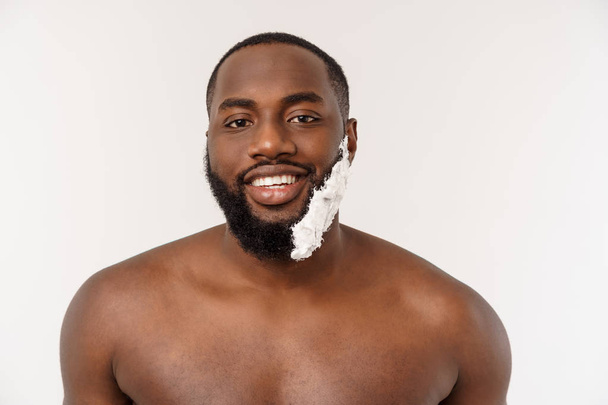 Αφρικανός Αμερικανός άνθρωπος επίχρισμα κρέμα ξυρίσματος στο πρόσωπο με βούρτσα ξυρίσματος. Ανδρική υγιεινή. Απομονωμένος σε λευκό φόντο. Πορτρέτο στούντιο - Φωτογραφία, εικόνα