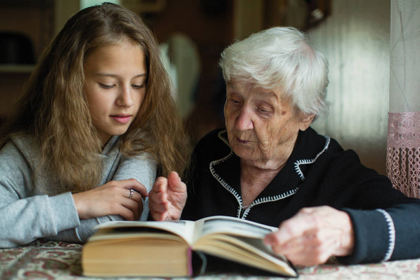 Старуха - бабушка с маленькой девочкой - внучка читает книгу
.  - Фото, изображение